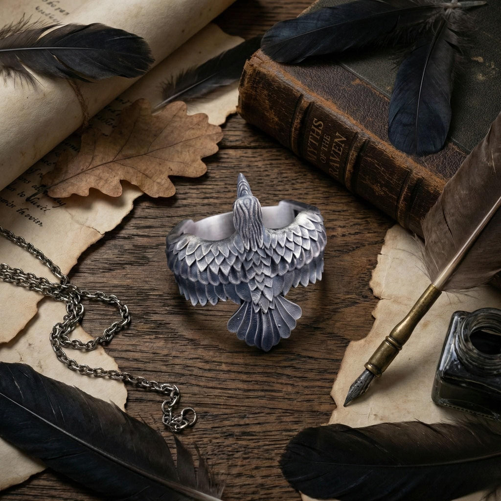 a silver bird-shaped bracelet, a pen, a book, and some feathers arranged on a wooden surface.
