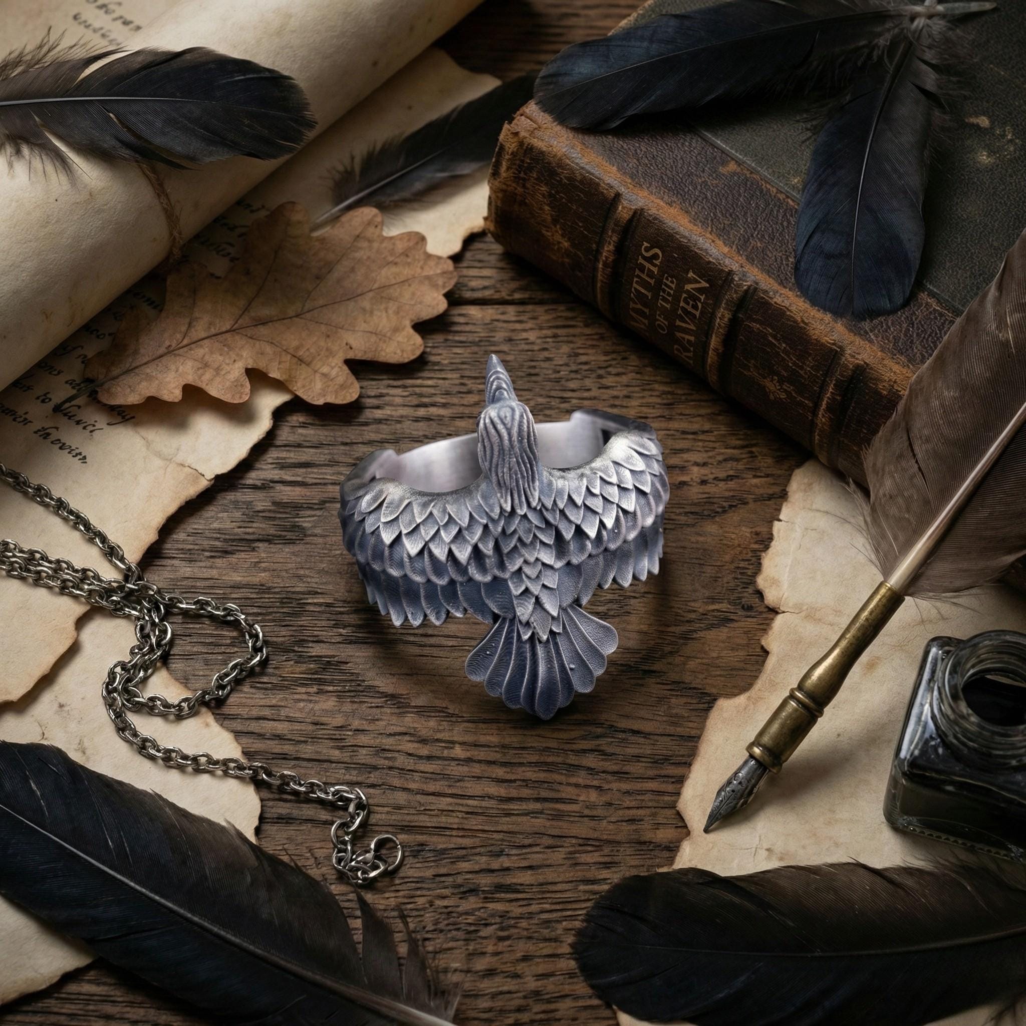 a silver bird-shaped bracelet, a pen, a book, and some feathers arranged on a wooden surface.