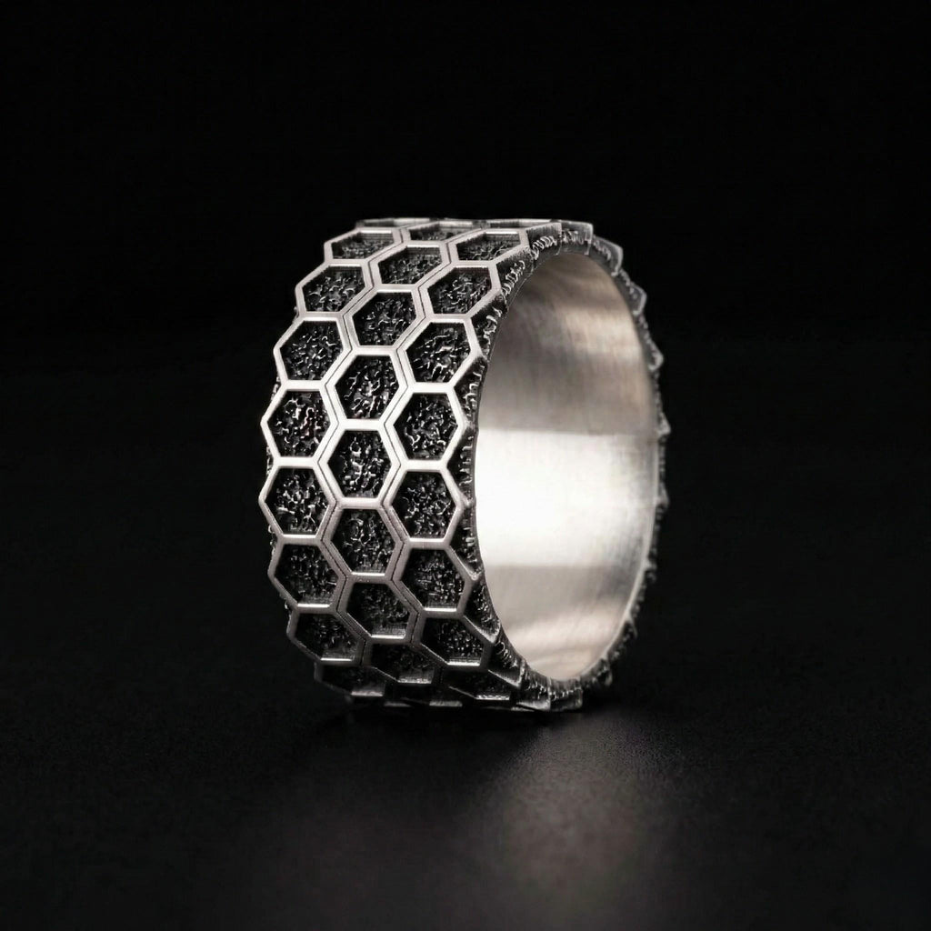 A silver ring with a honeycomb pattern design, featuring small black hexagonal shapes.