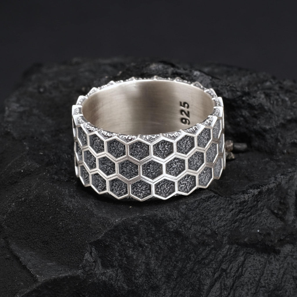 A silver ring with a honeycomb pattern sits on a dark surface.