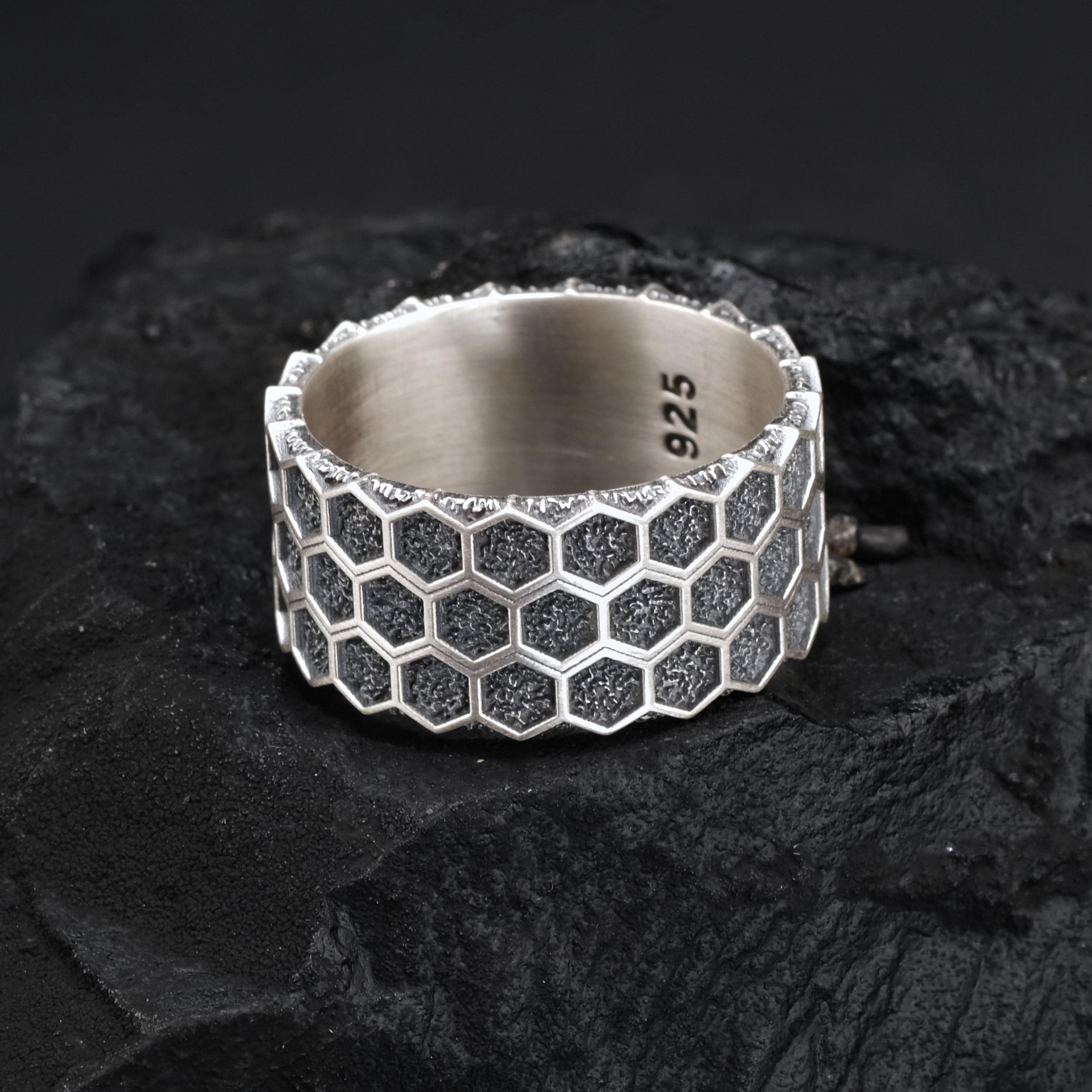 A silver ring with a honeycomb pattern sits on a dark surface.
