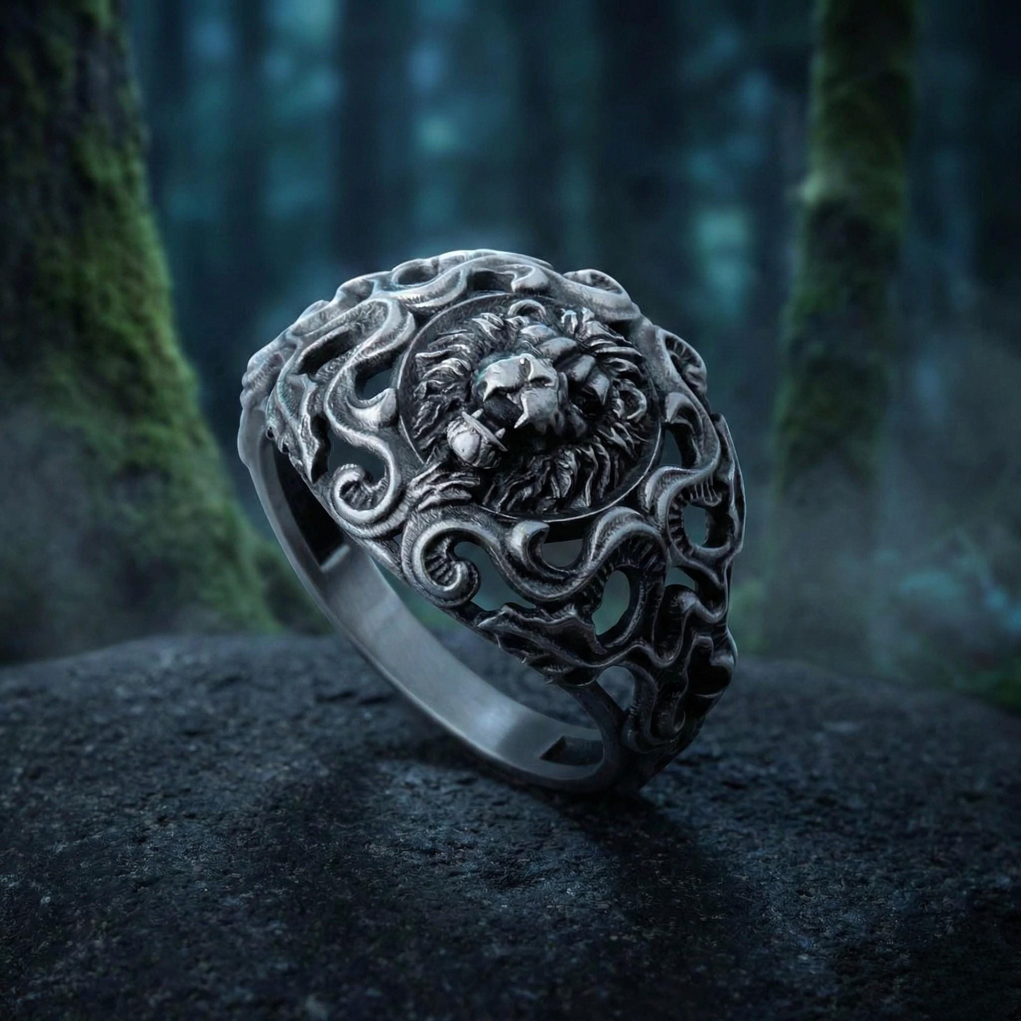 A silver ring with an intricate design featuring a lion's head, set against a dark, mossy background.