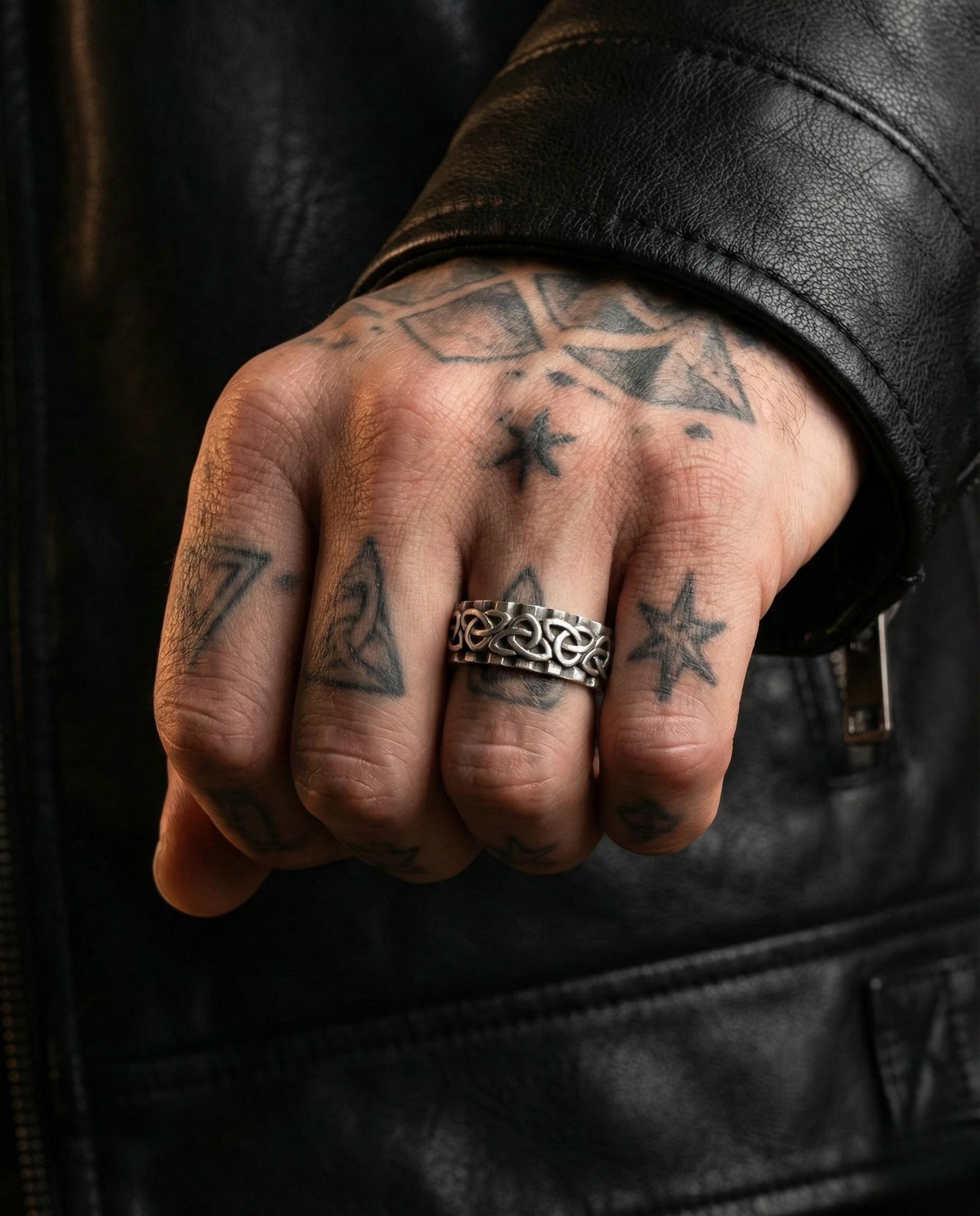 A close-up of a person's hand with multiple tattoos on the fingers and a ring on the ring finger.