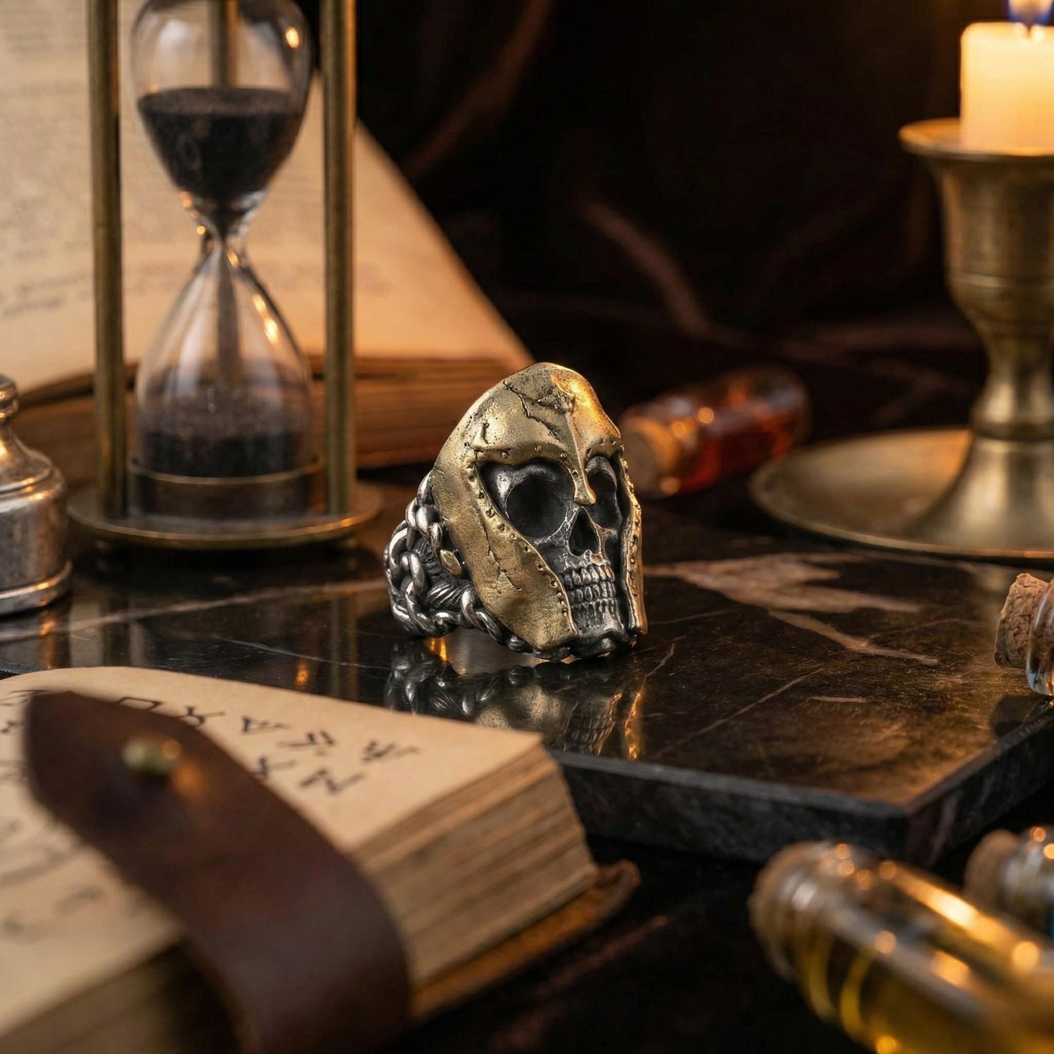 a ring with a skull design, a book, a candle, and an hourglass on a table.