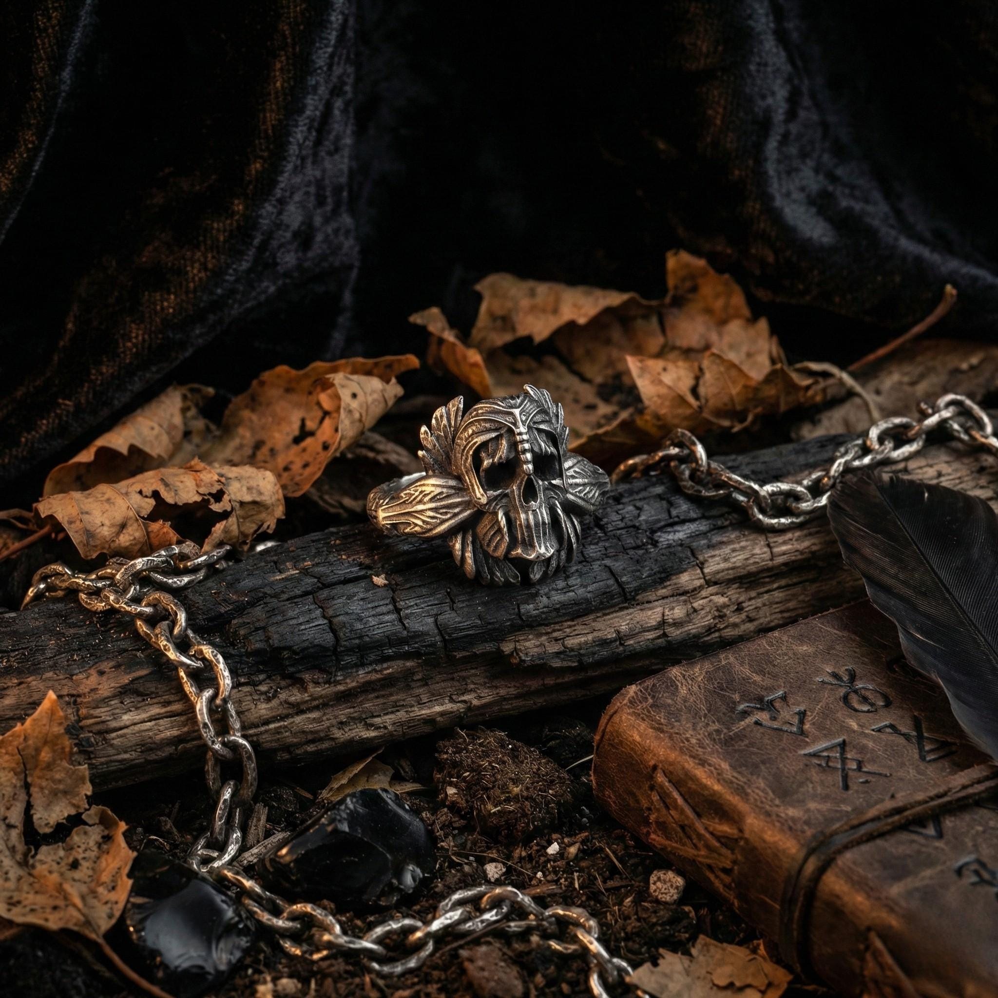 a silver ring with a skull design, surrounded by a chain, leaves, and a book with mysterious symbols on its cover.