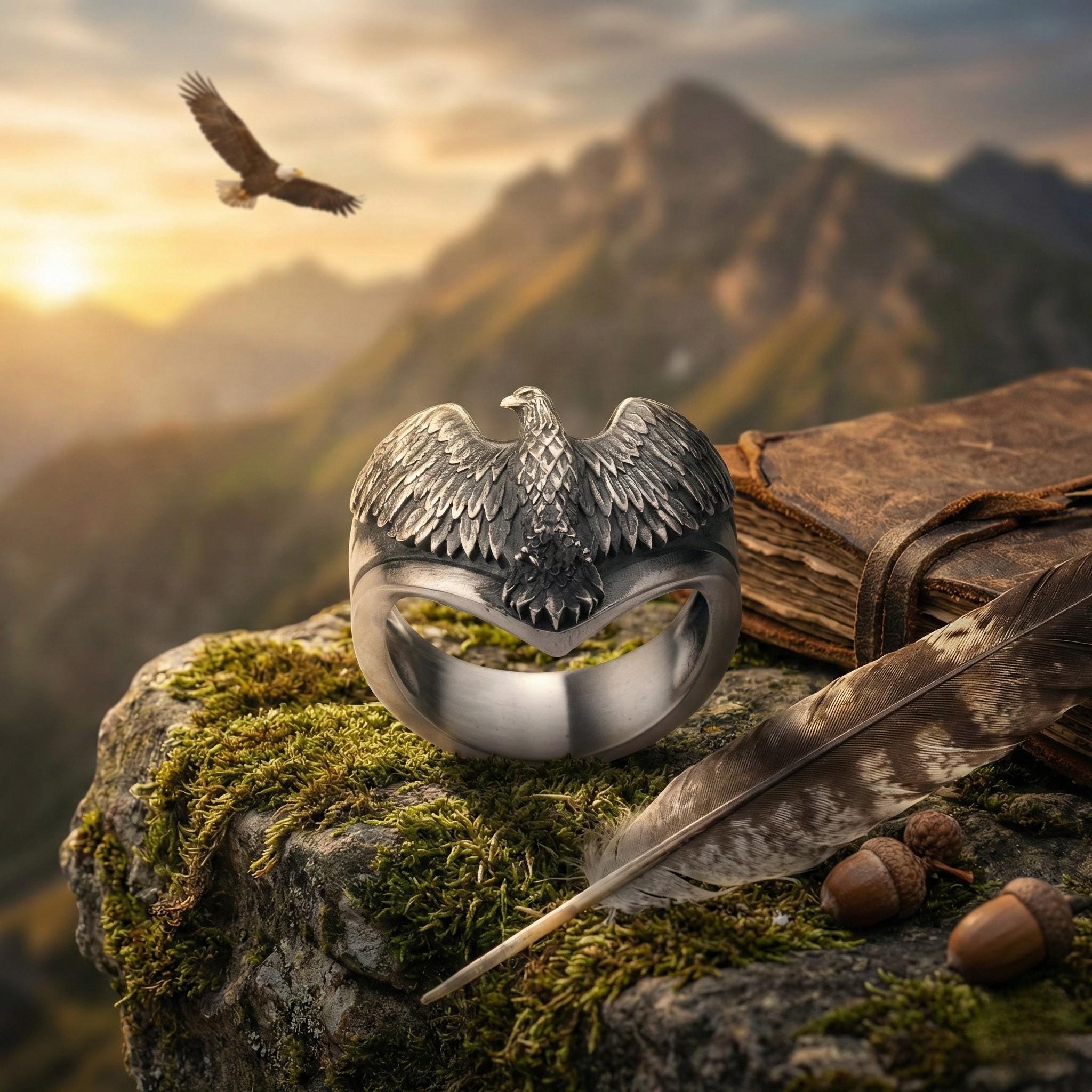 a ring with a bird design, a feather, and some acorns, all set against a backdrop of mountains and a sunset.