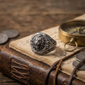 a ring with a lion's head design, a compass, and a leather-bound book or notebook on a wooden surface.