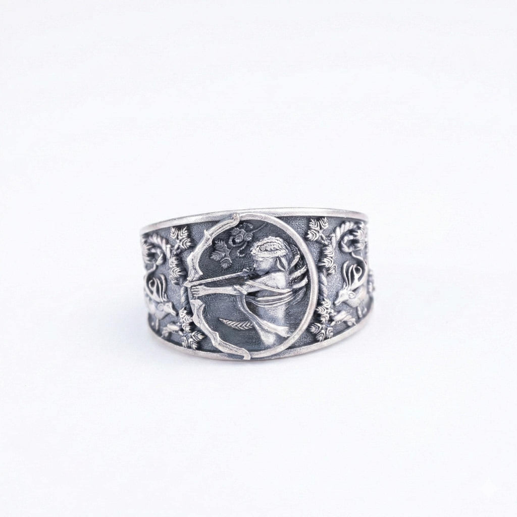 A silver ring with an intricate engraved design featuring a central figure surrounded by floral and animal motifs.