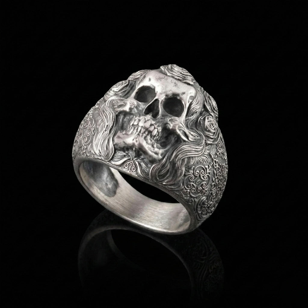 A silver ring with an intricate design featuring a skull and floral elements.
