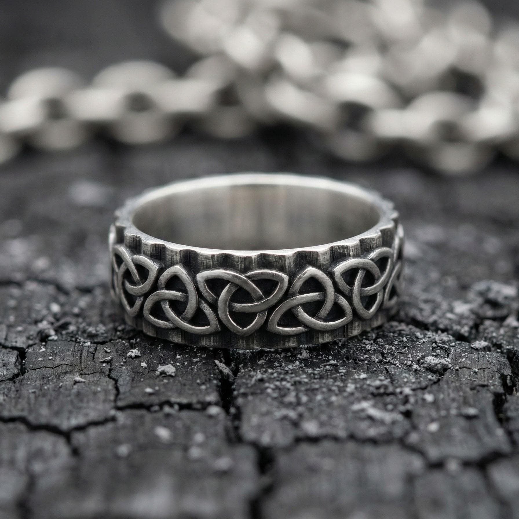 A silver ring with a Celtic knot design sits on a cracked, dark surface.
