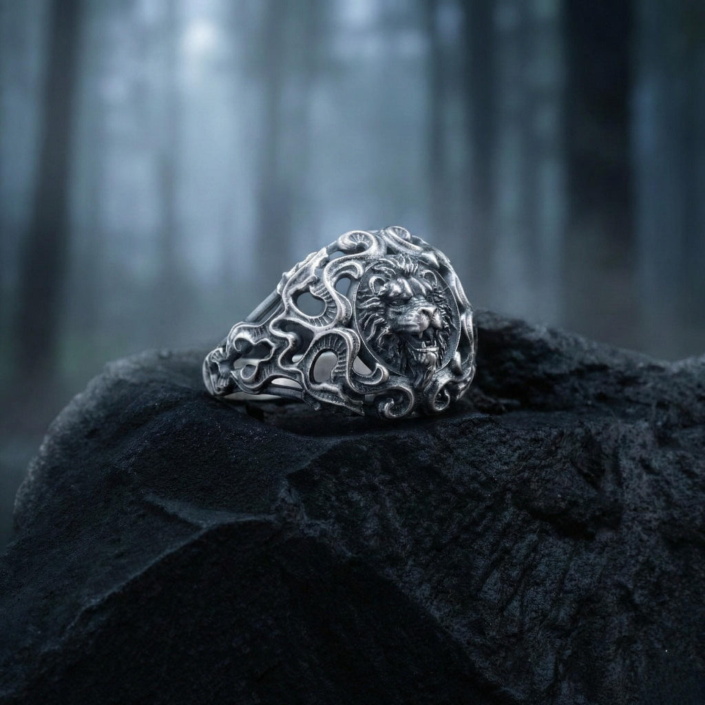 A silver ring with an intricate design sits on a black rock in a dark, wooded area.
