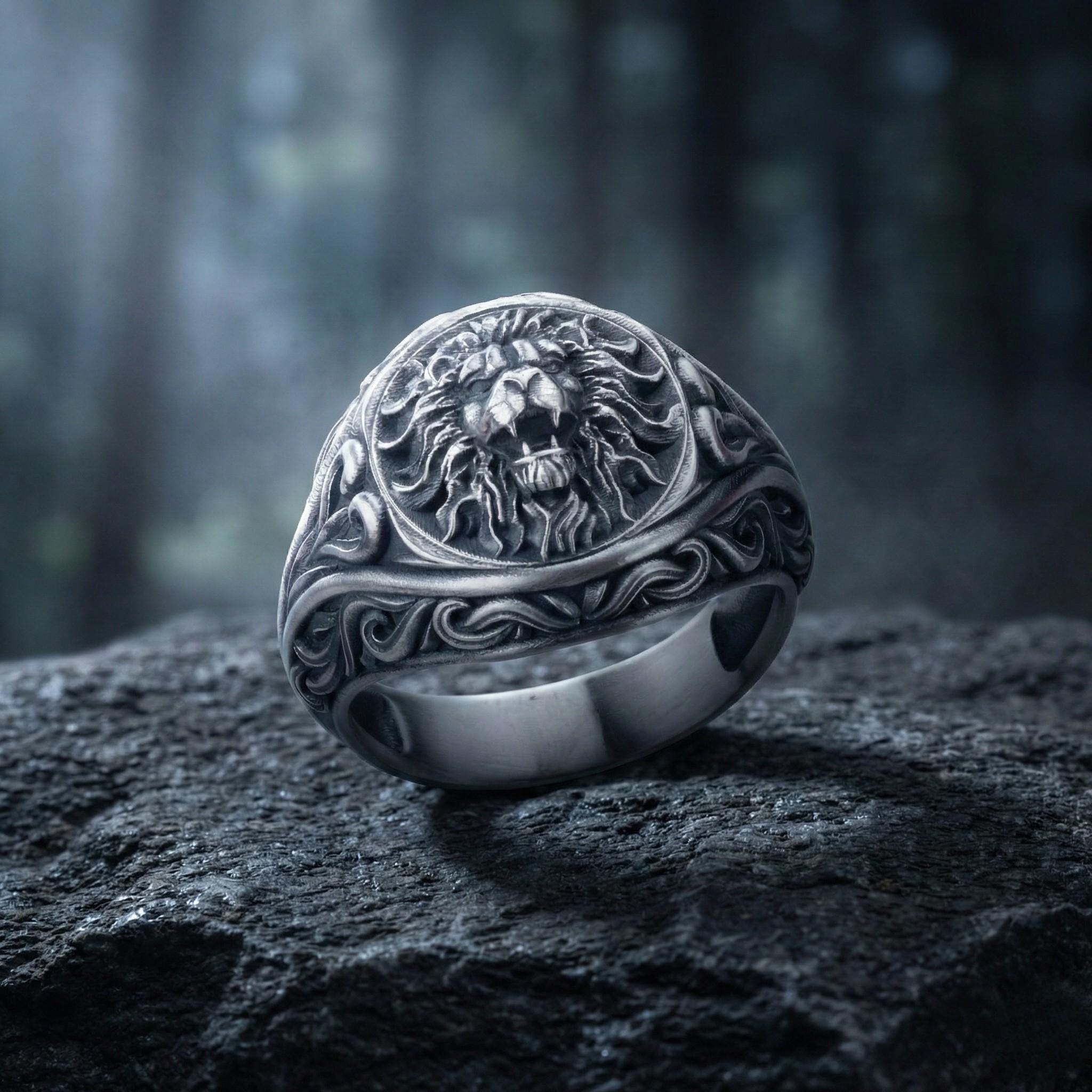 A silver ring with an intricate lion head design is resting on a rock.