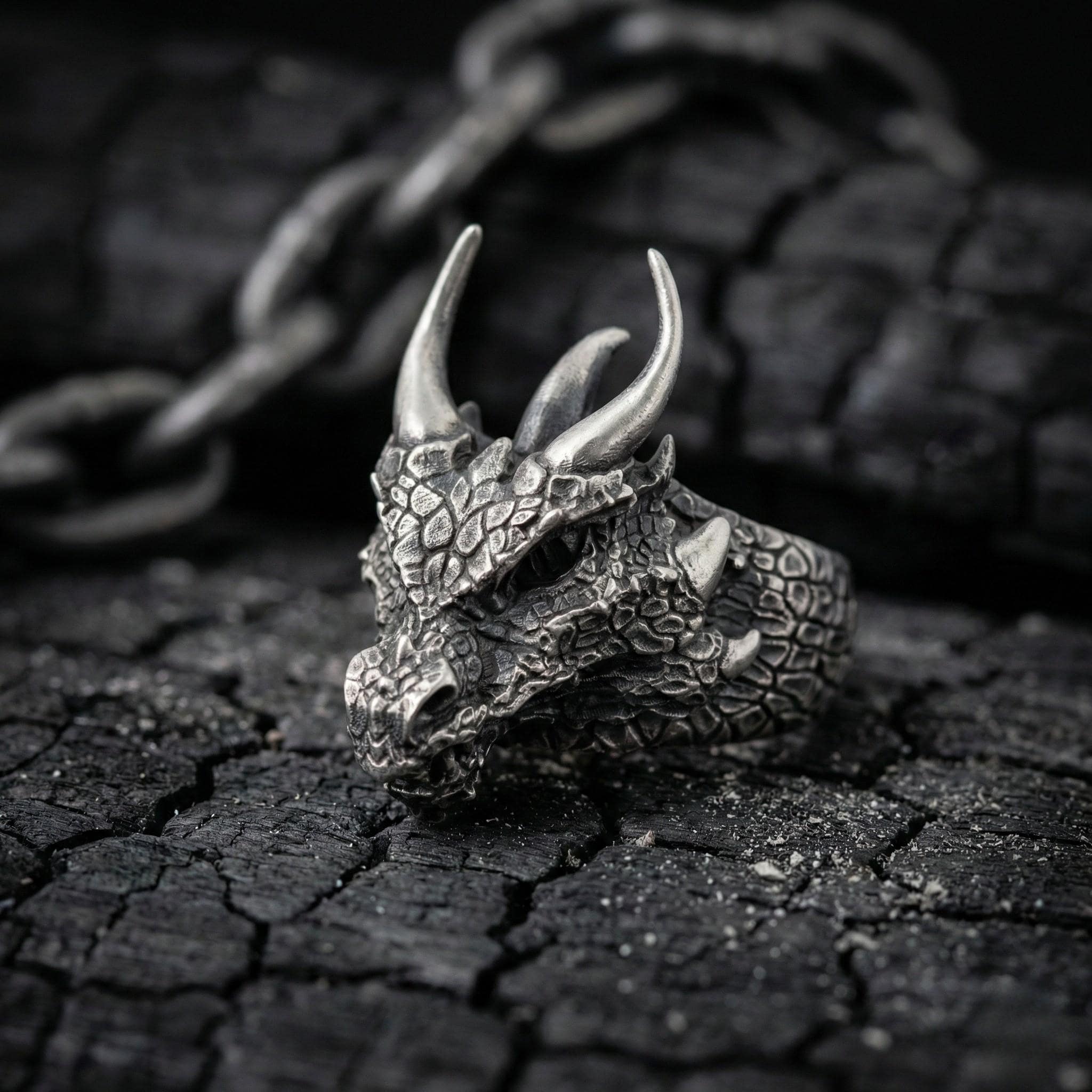 A close-up image of a silver dragon head ring with sharp horns, resting on a cracked and weathered surface.