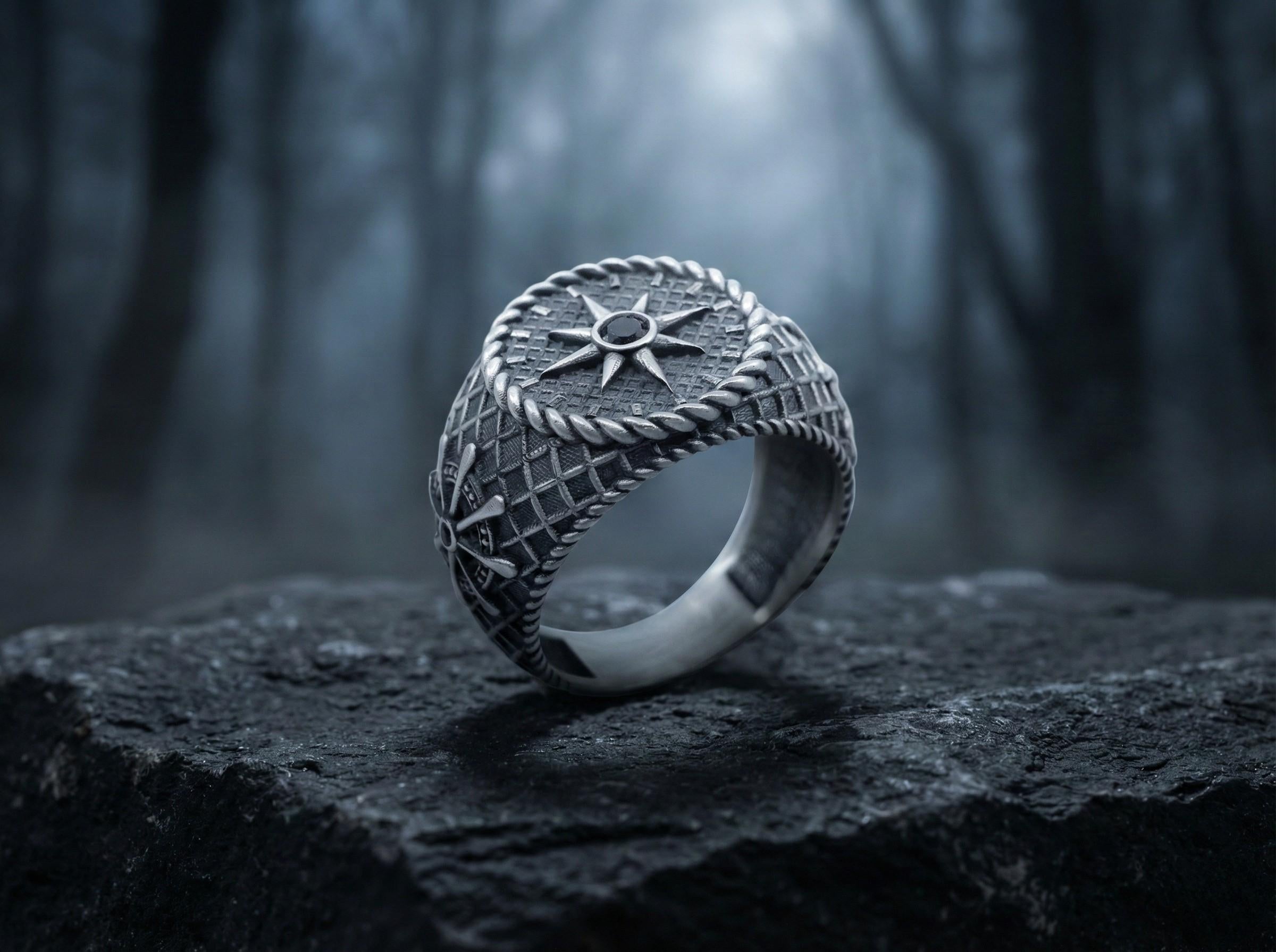 A silver ring with a star design sits on a rock in a dark, wooded area.
