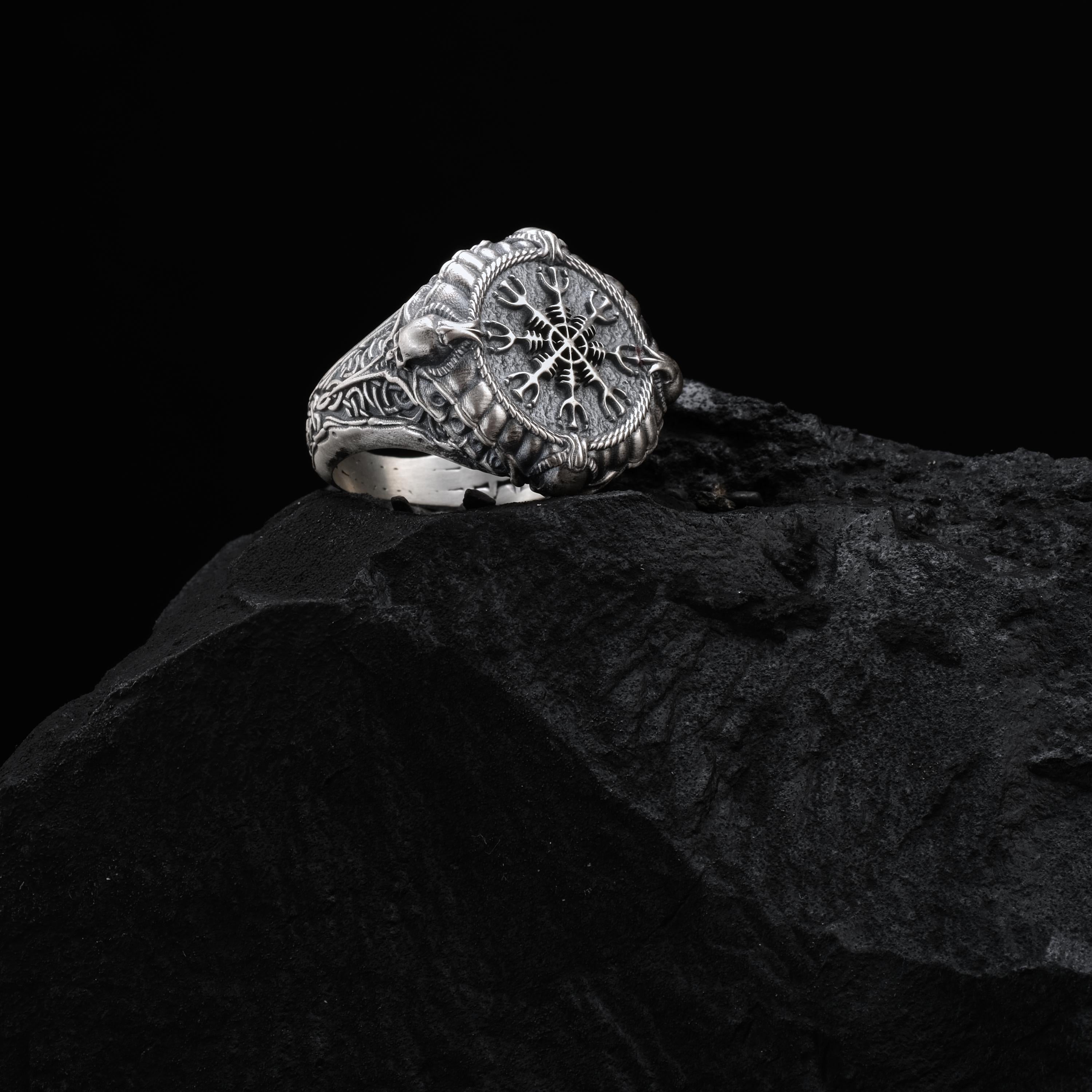 A silver ring with intricate designs sits atop a dark, rocky surface.