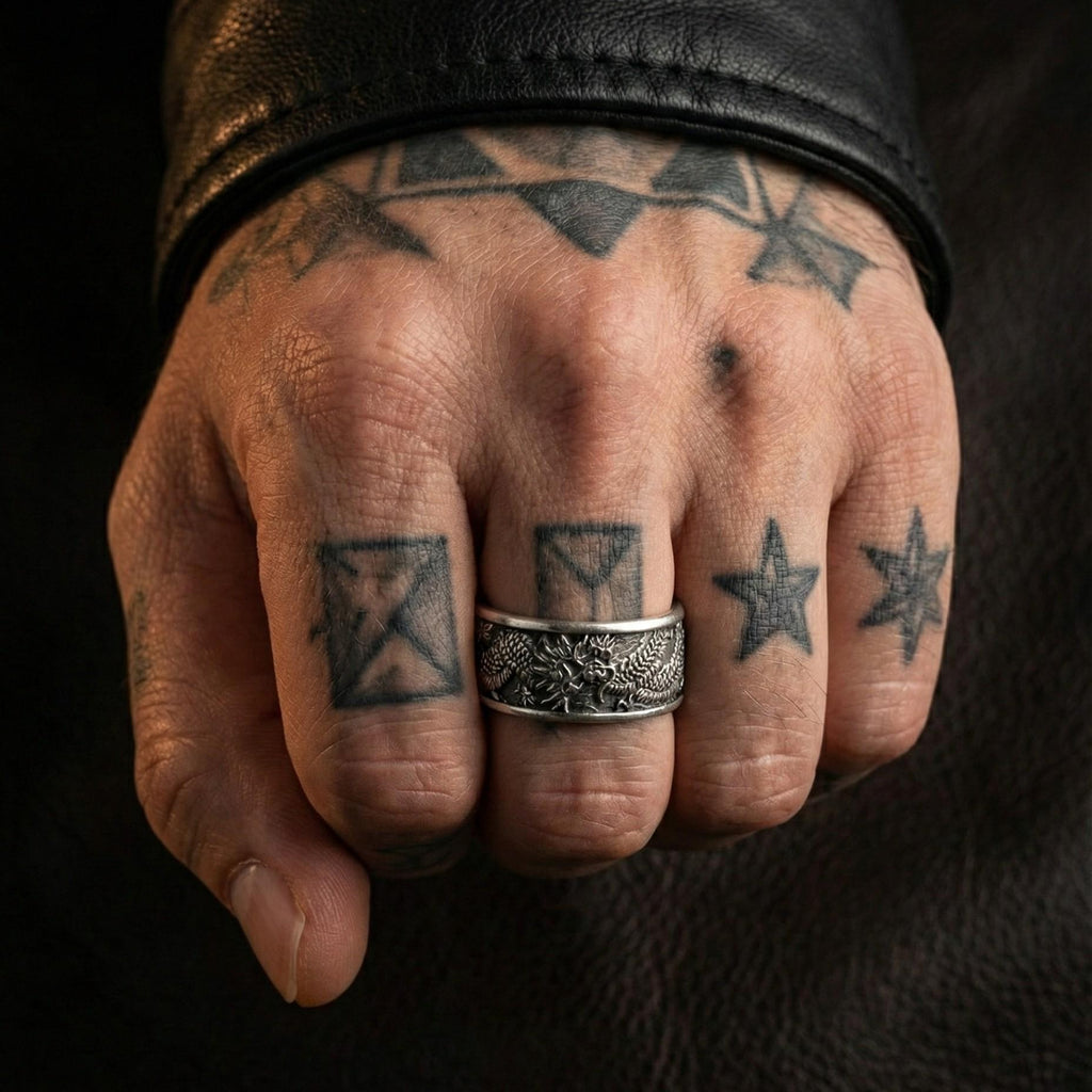 A close-up of a person's hand with multiple tattoos on the fingers and a silver ring on the ring finger.