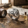 a silver ring with intricate gears and mechanical elements, surrounded by various mechanical parts and tools, such as a magnifying glass, a bottle, and a set of gears, all arranged on a wooden surface.