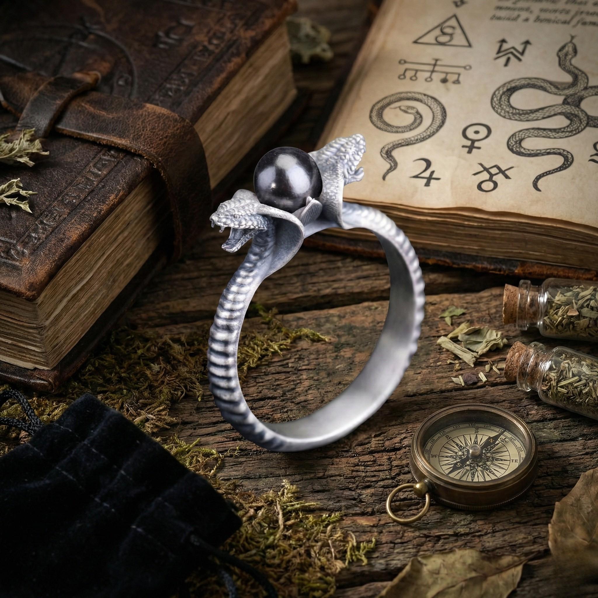 a silver ring with a snake design, a book, a compass, and some herbs or spices on a wooden surface.