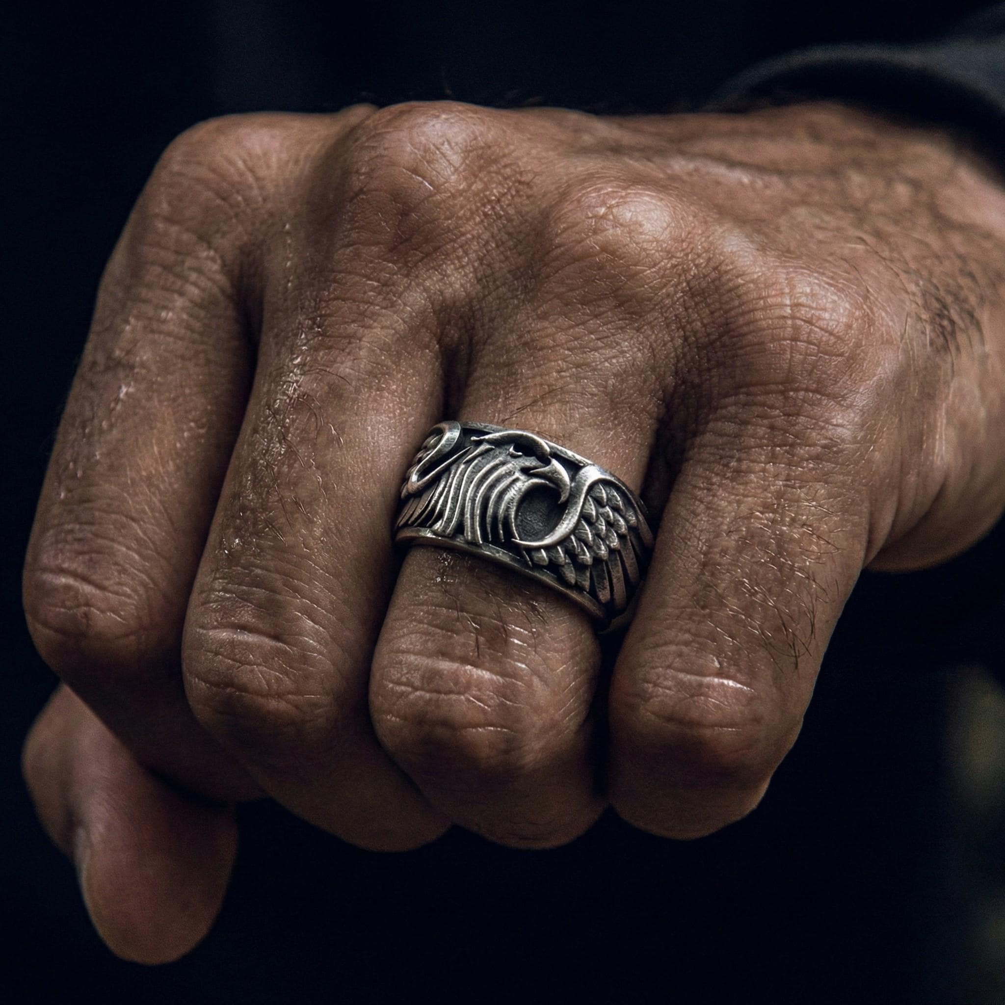 A close-up of a person's hand wearing a silver ring with an intricate design.