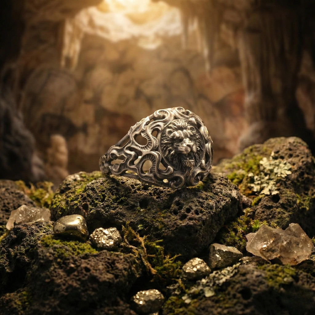 A silver ring with an intricate design sits atop a pile of rocks and minerals in a cave-like setting.