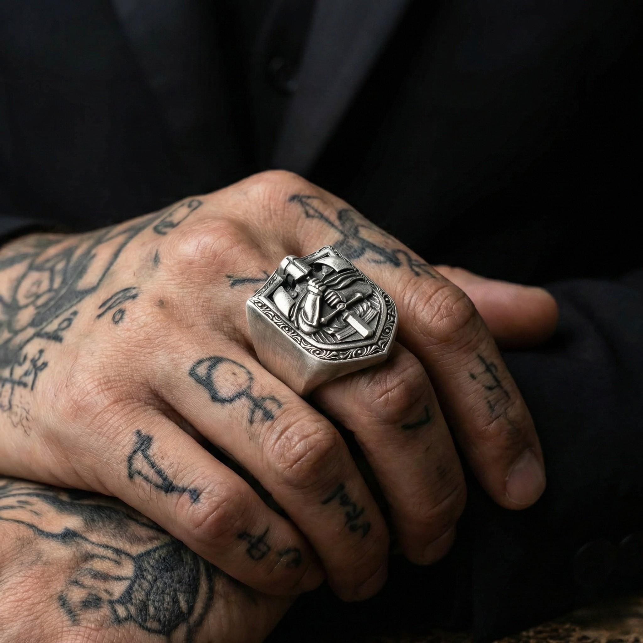 A close-up image of a person's hand wearing a large silver ring with a decorative design.