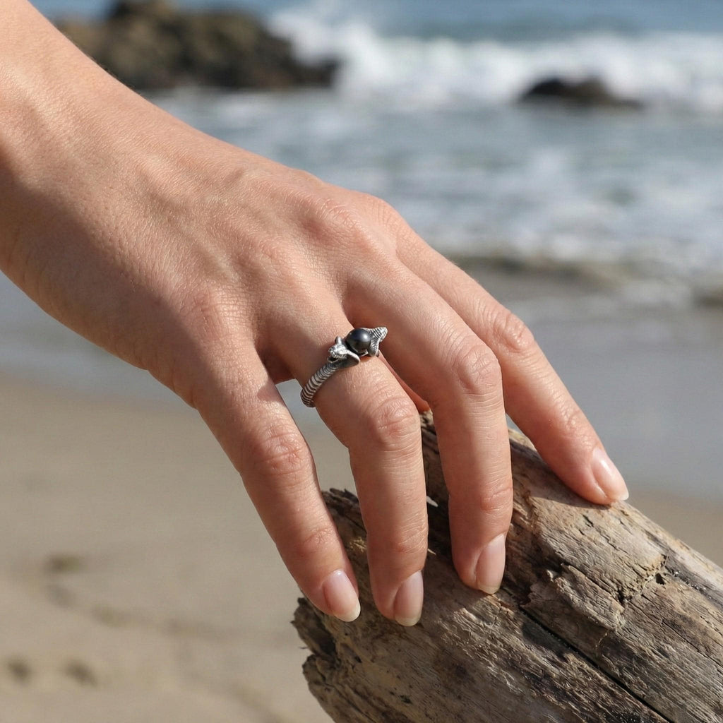 A close-up of a hand wearing a ring, with a blurred background of the ocean and a wooden log.