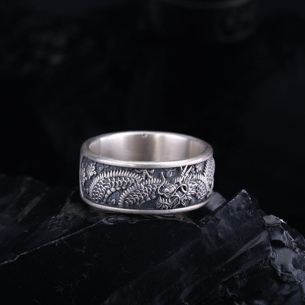 A silver ring with an intricate dragon design on a black background.