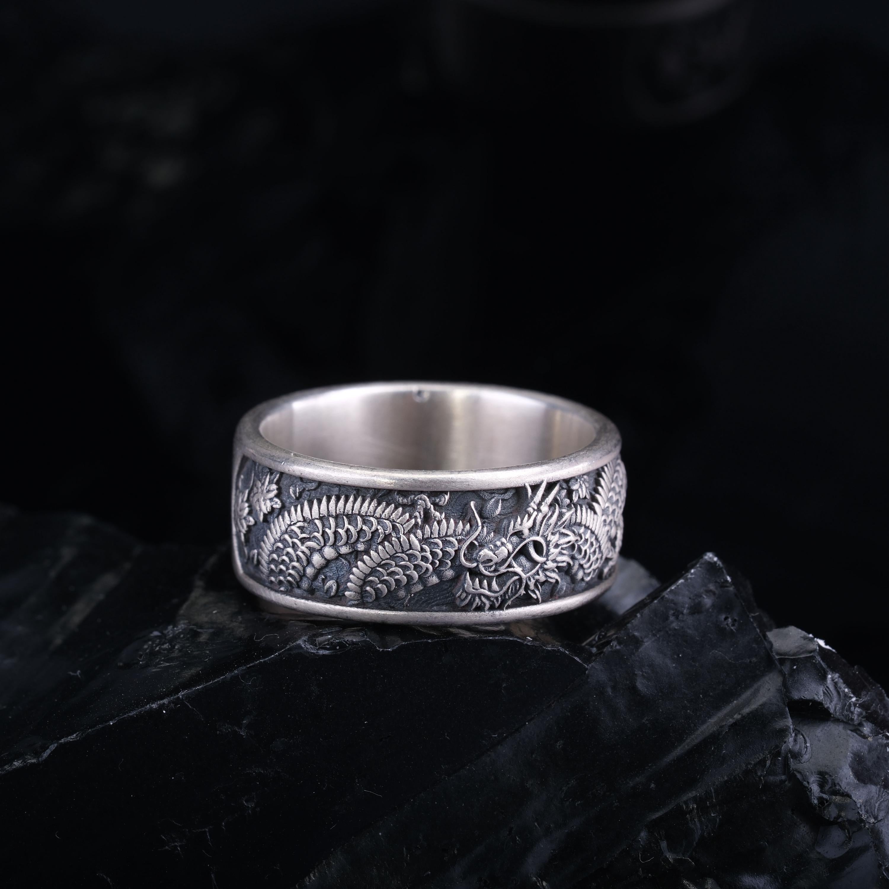 A silver ring with an intricate dragon design on a black background.