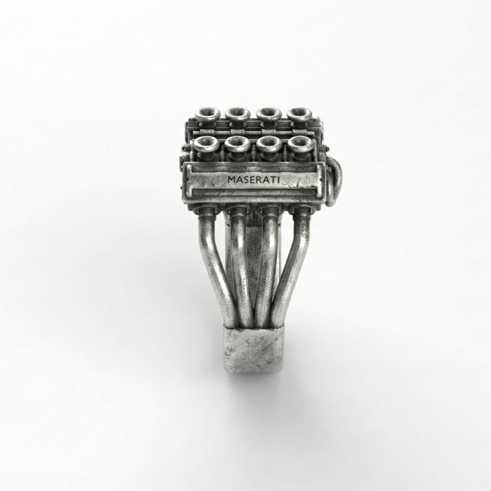 A silver ring with a detailed engine design, featuring multiple pipes and components.