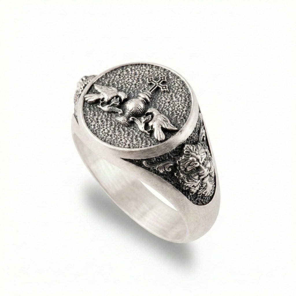 A silver ring with an intricate design featuring a cross, a lion, and a bird.