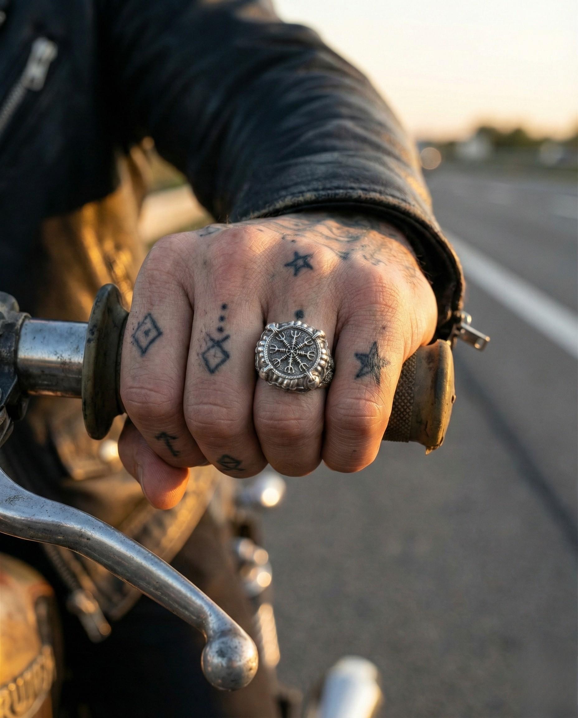A close-up of a person's hand wearing a large ring, with tattoos visible on the fingers.