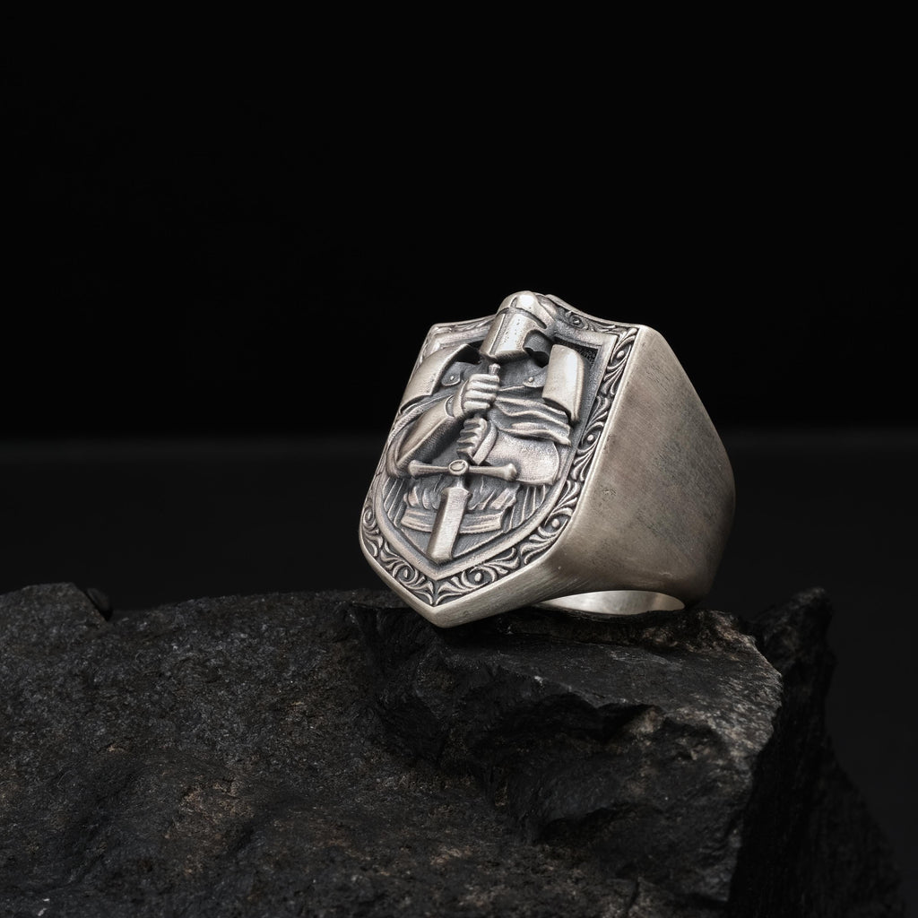 A silver ring with an embossed design on a rock.