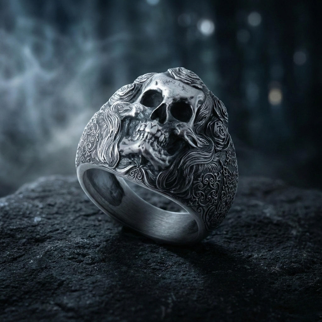 A silver ring with an intricate design featuring a skull and floral elements, set against a dark, moody background.