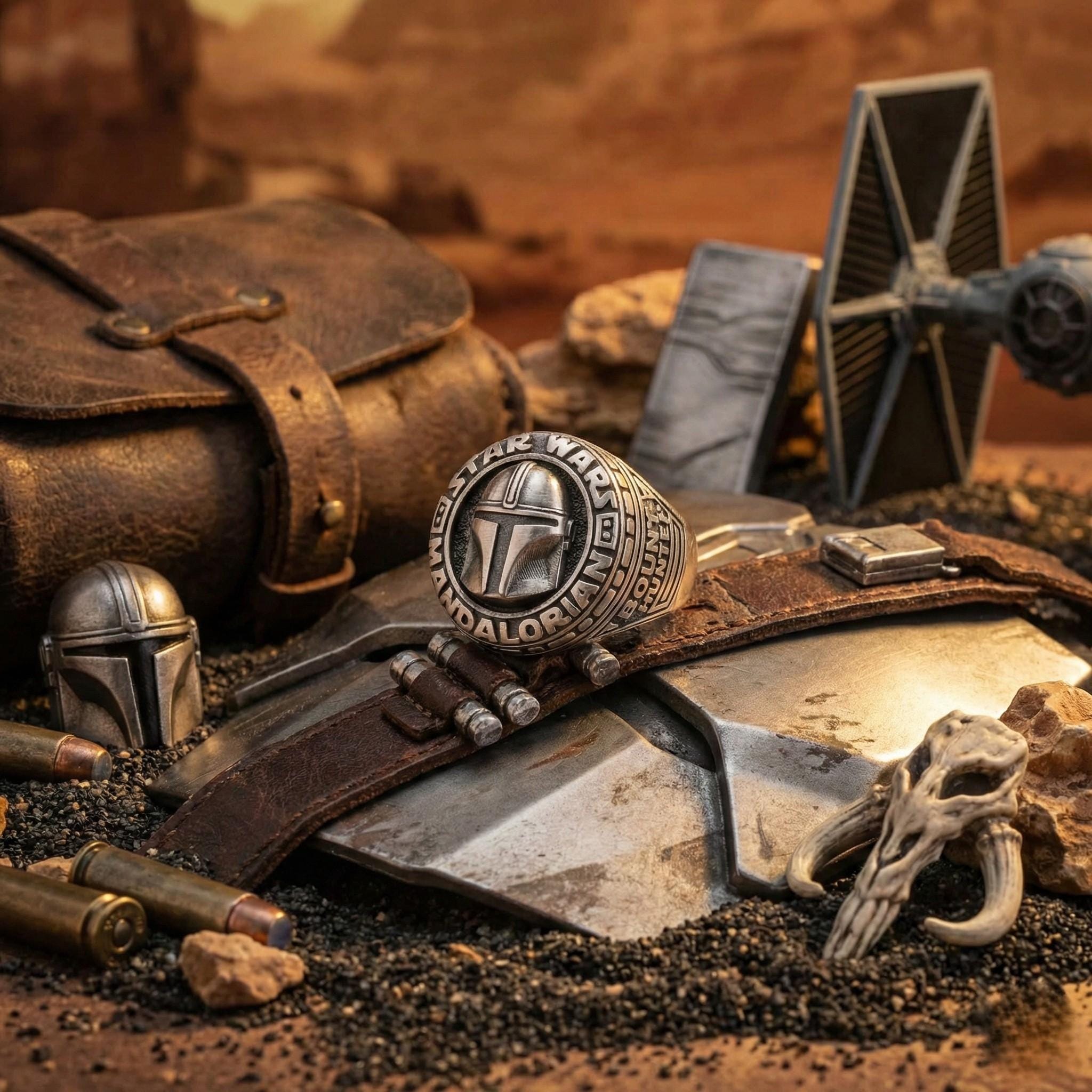 various Star Wars-themed items, including a ring, a helmet, a skull, and a TIE fighter jet, all arranged on a surface with sand and rocks.