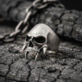 A silver skull ring with sharp teeth is resting on a rough, cracked surface.