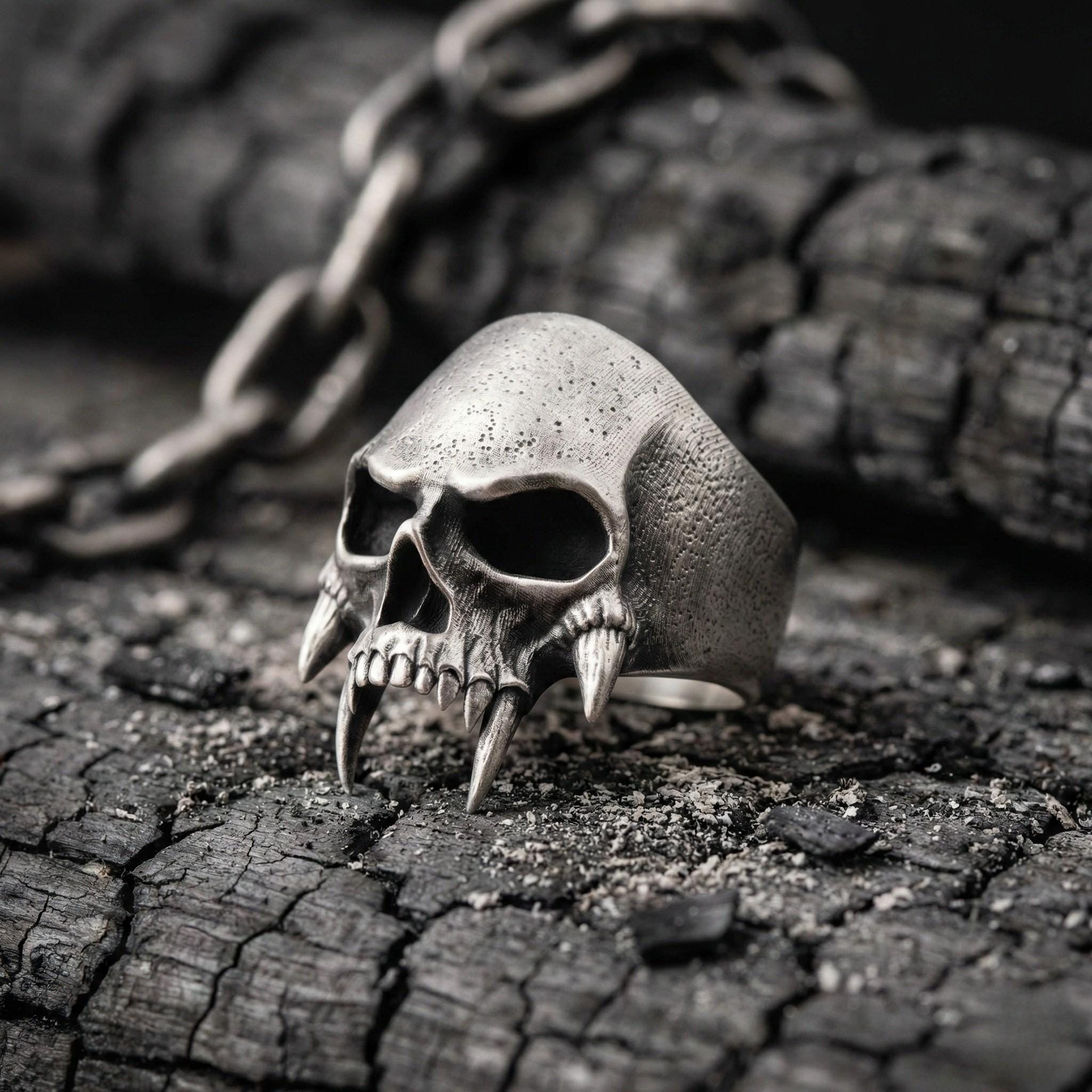 A silver skull ring with sharp teeth is resting on a rough, cracked surface.