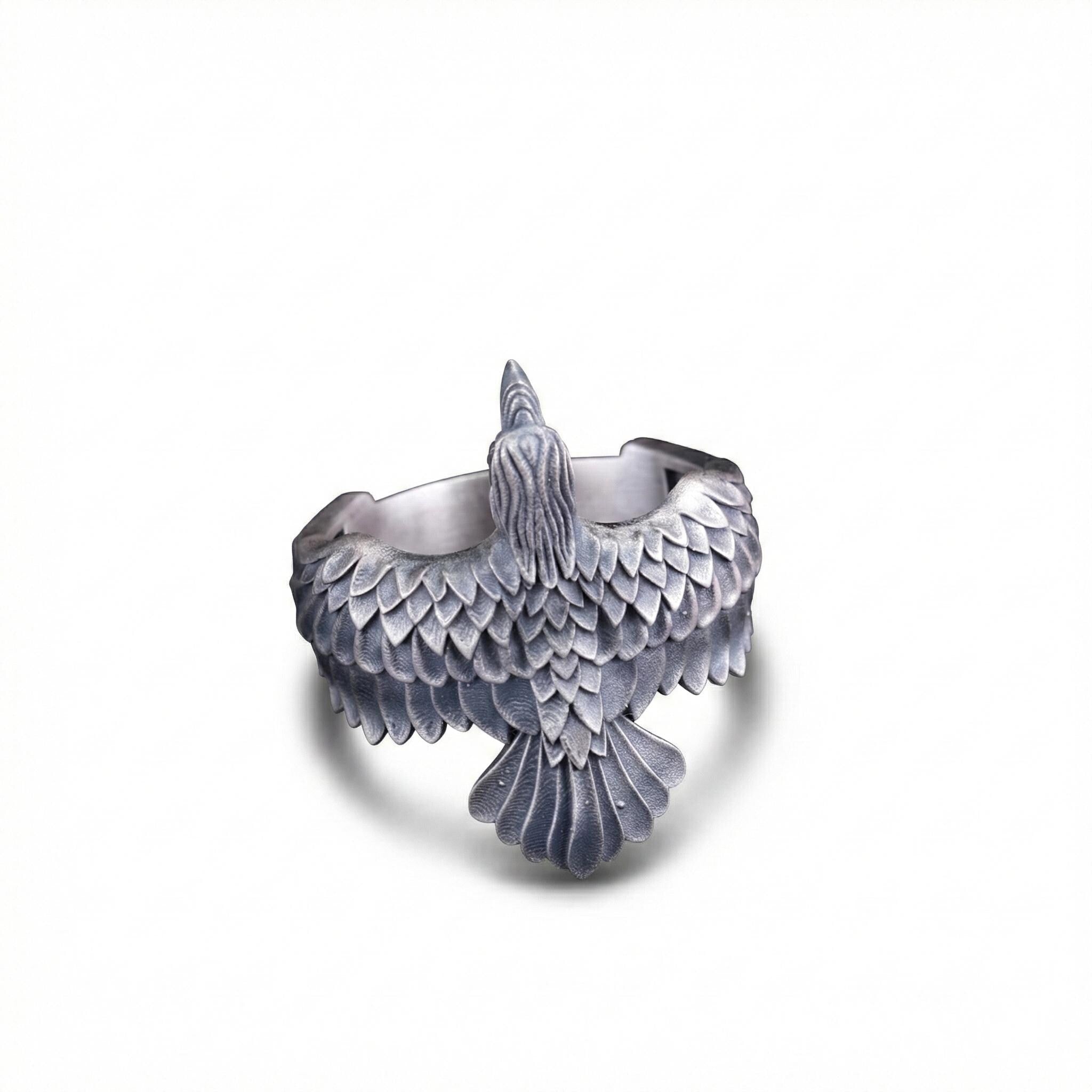 A silver-colored metal ring with a detailed bird-like design on it.