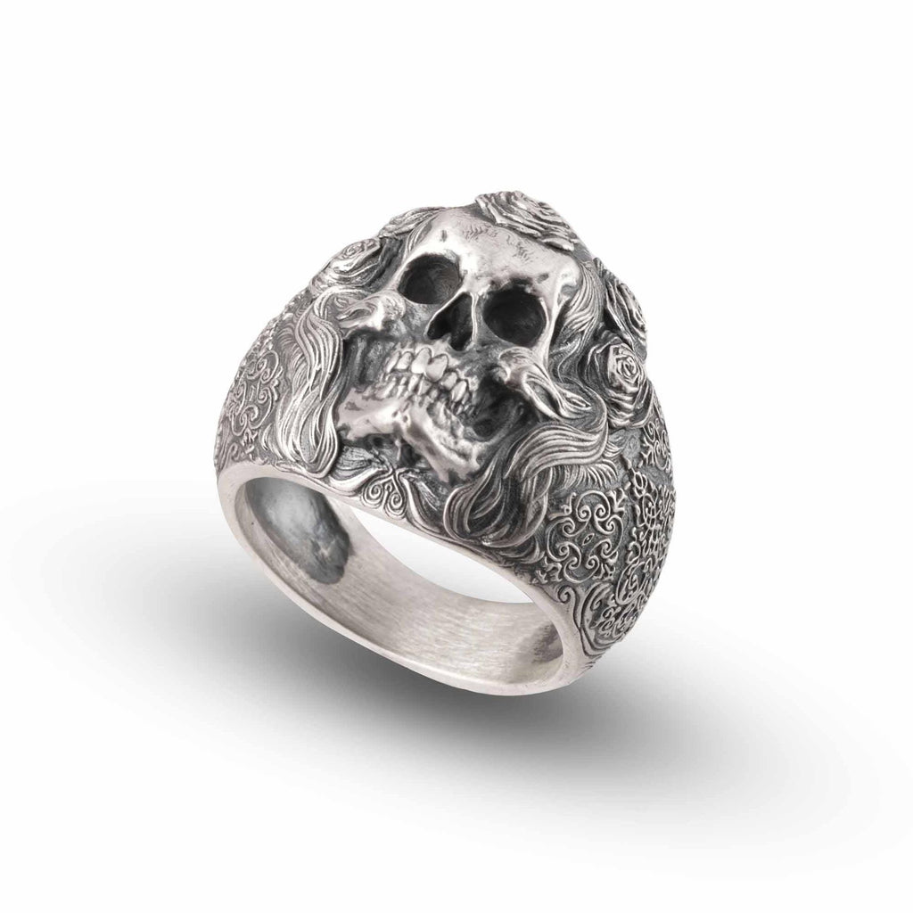 A silver ring with an intricate design featuring a skull and floral elements.