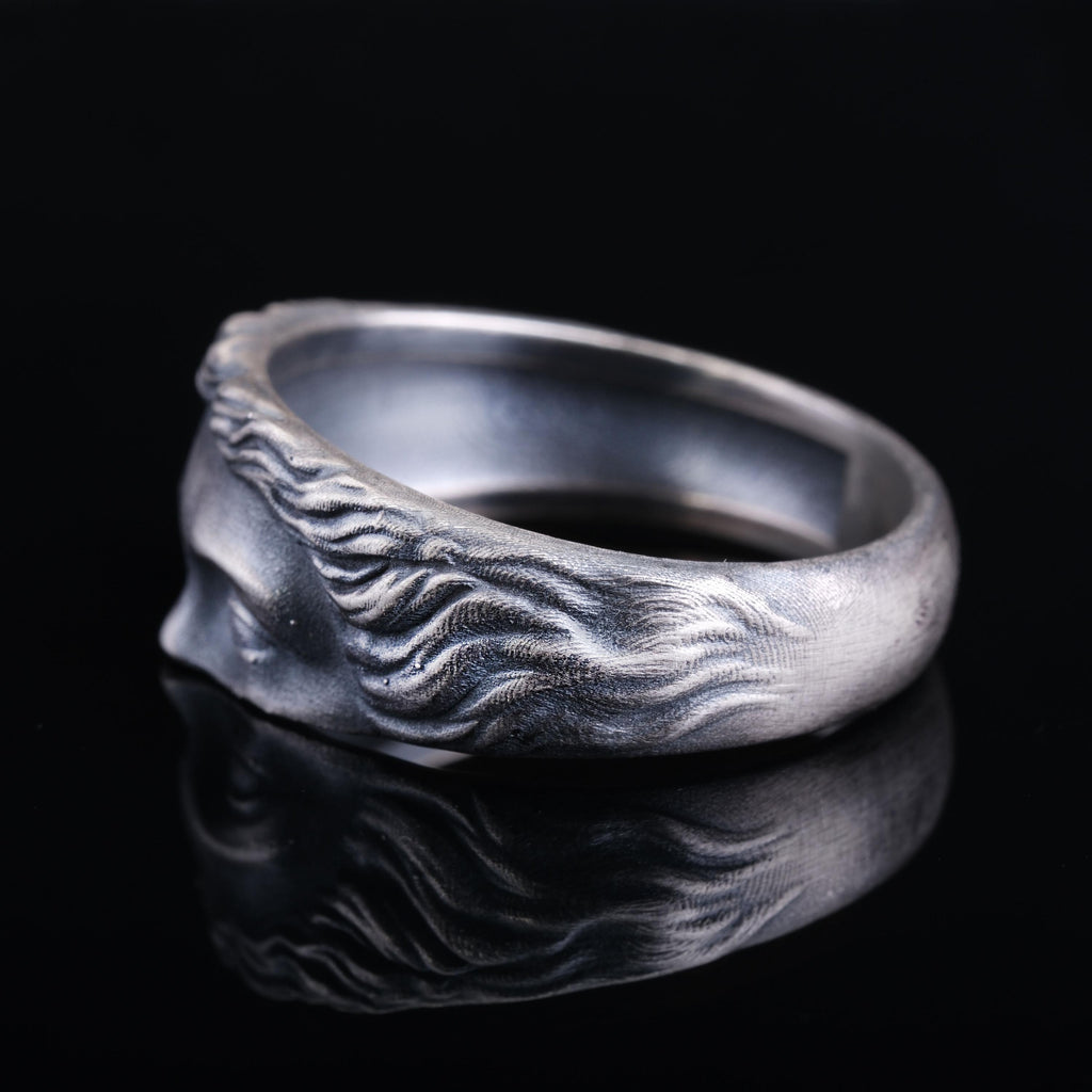 A silver ring with a detailed design, reflecting on a dark surface.