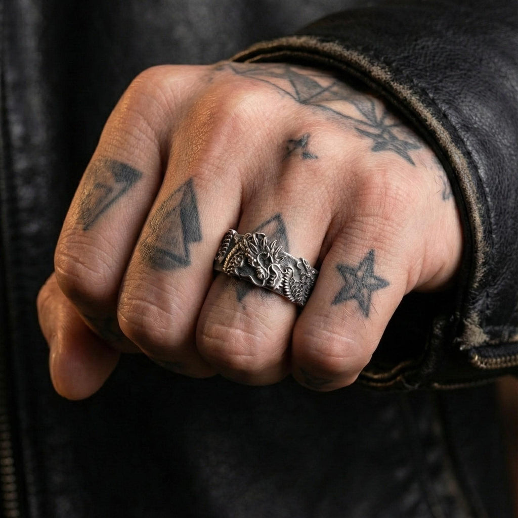 A close-up of a person's hand wearing a silver ring with a dragon design, with tattoos visible on the fingers.
