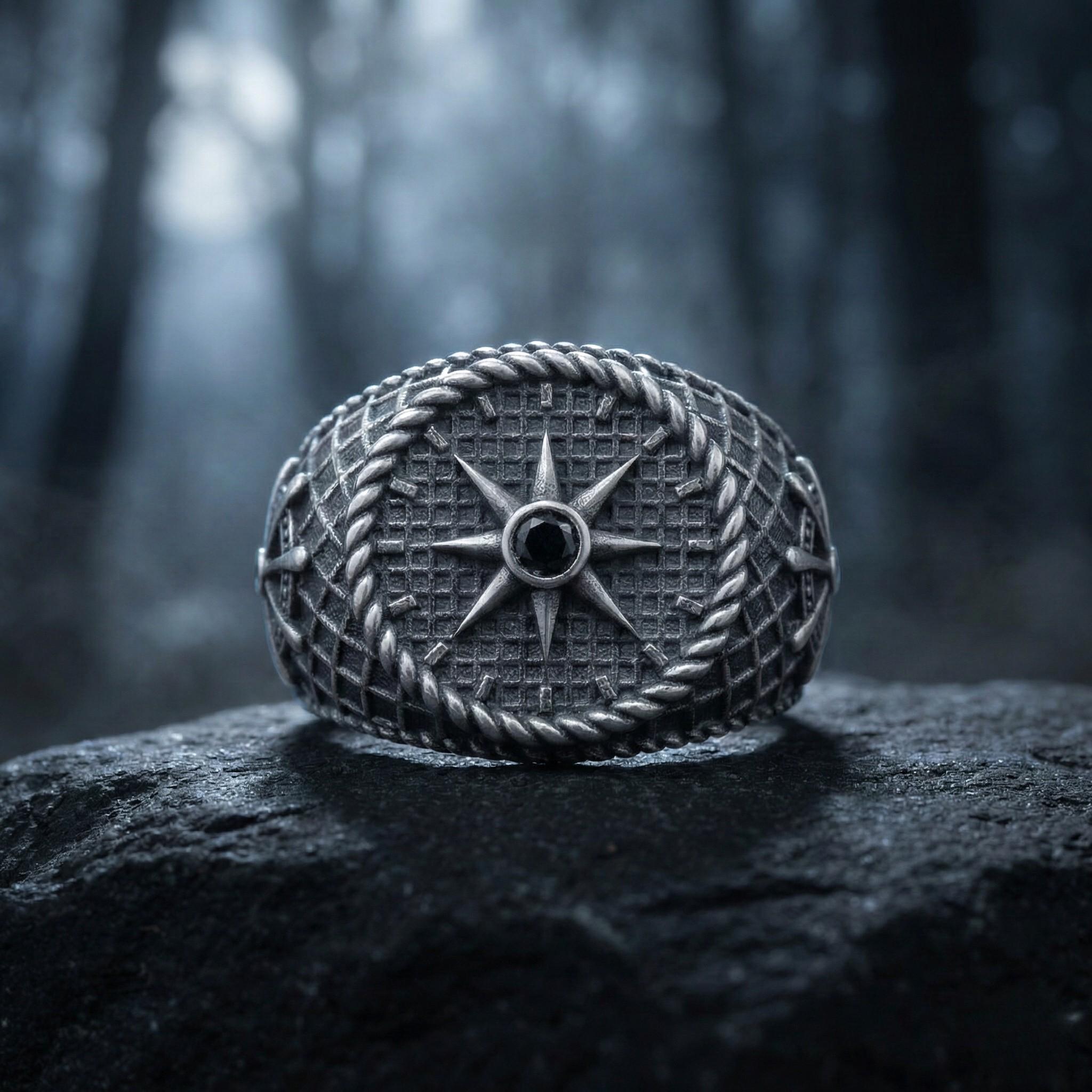 A silver ring with a compass design sits on a rock in a dark, wooded area.