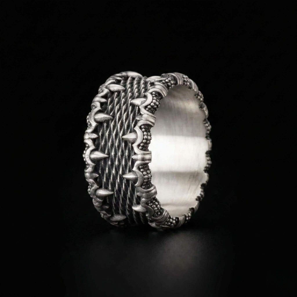 A silver ring with an intricate, textured design featuring spikes or spikes and a textured pattern around the edge.