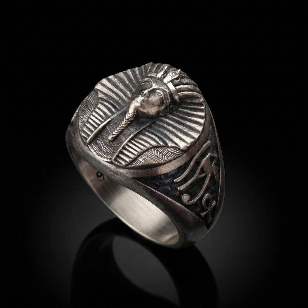 A silver ring with an embossed design featuring a stylized human head or face, possibly a pharaoh or deity, against a black background.