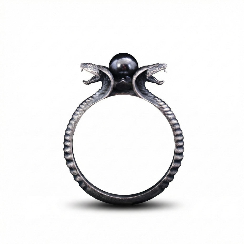 A ring with a snake design on top, featuring two snakes with their heads open, and a pearl at the center.