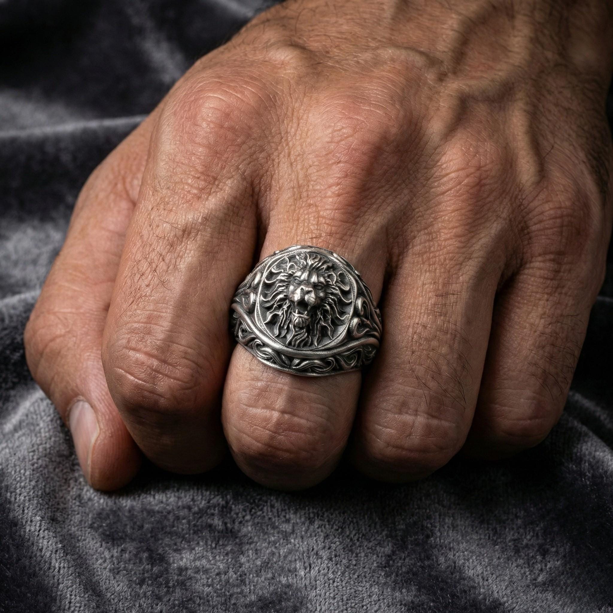 A close-up image of a hand wearing a silver ring with an intricate design.