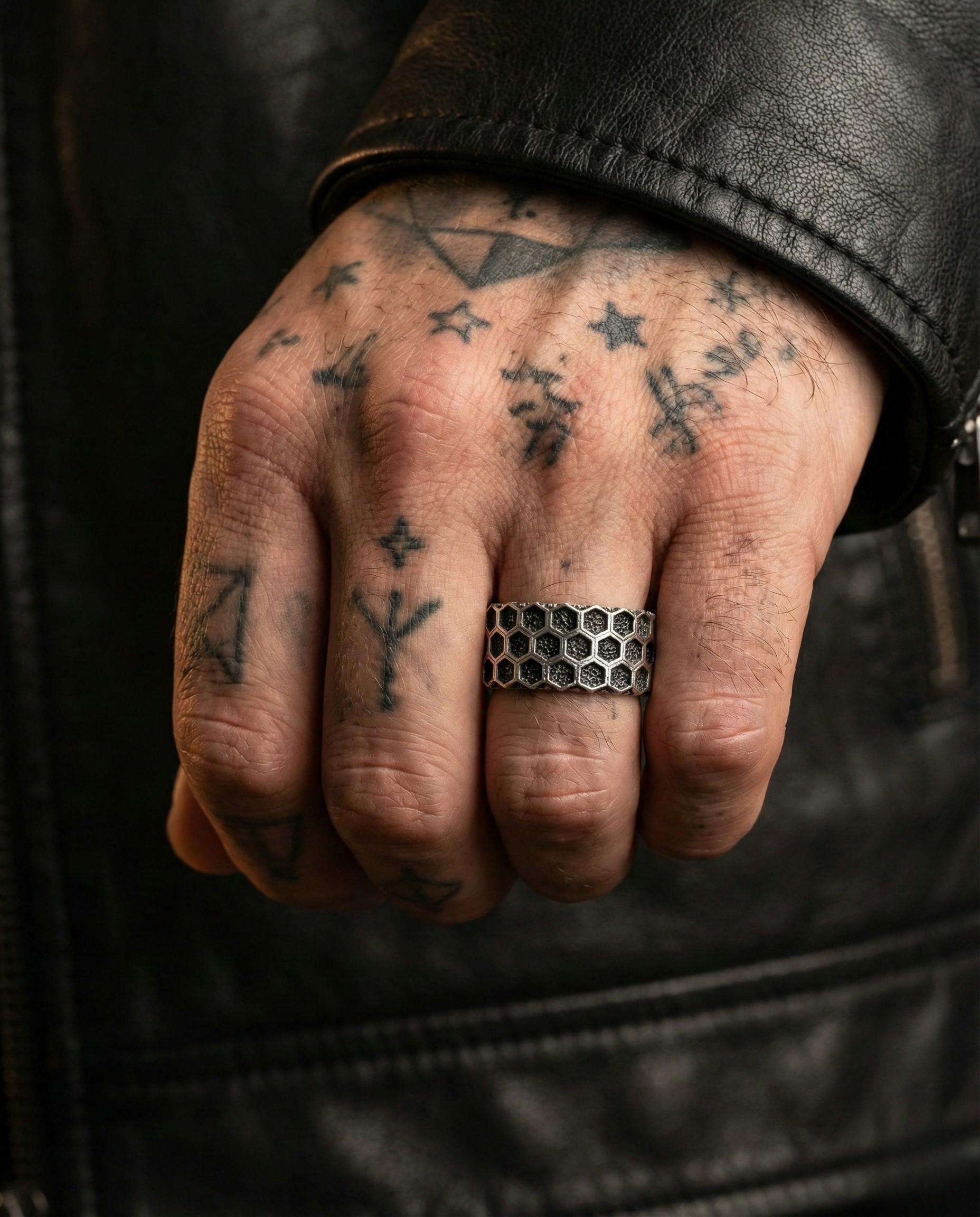 A close-up of a person's hand with tattoos on the fingers and a ring on the ring finger.