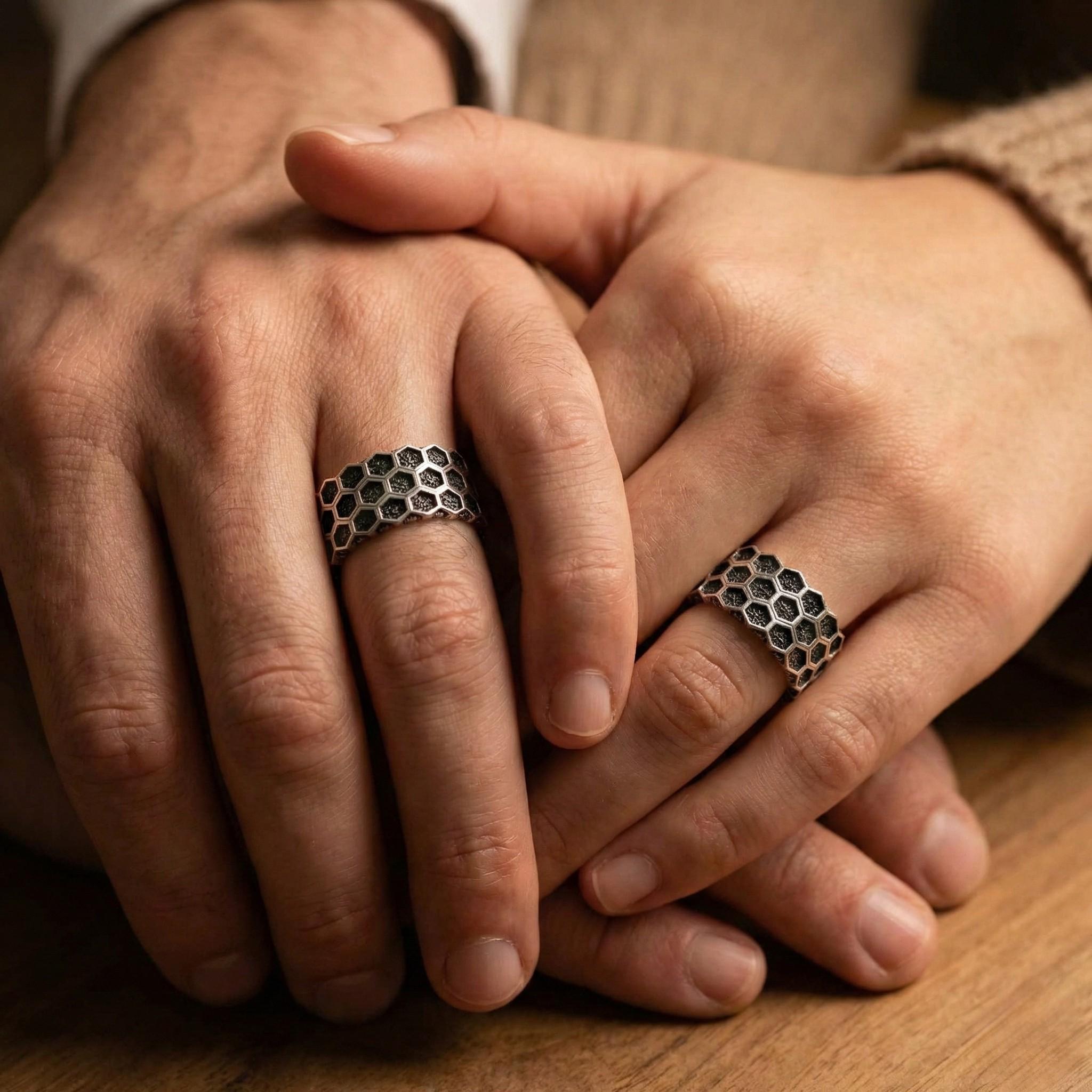A close-up image of two hands wearing silver rings with a honeycomb pattern.