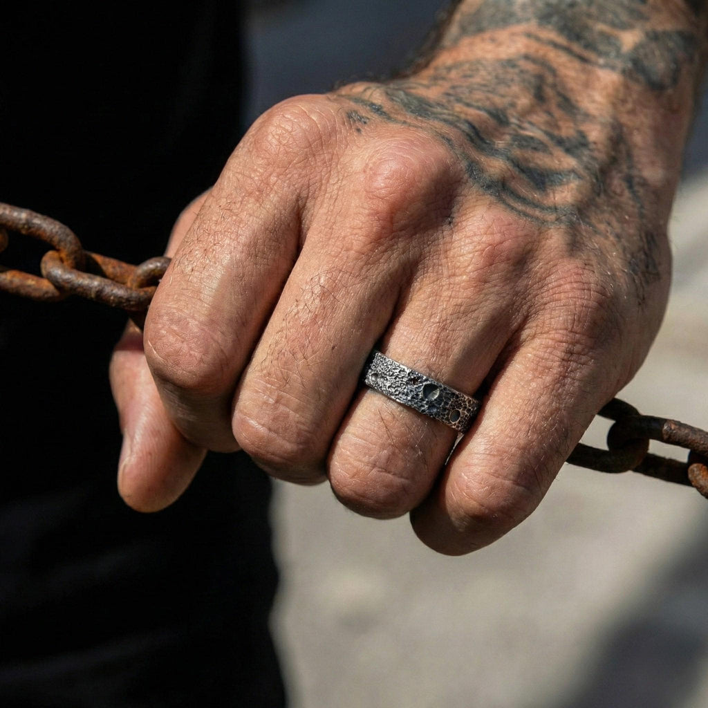 A close-up of a person's hand wearing a silver ring, holding onto a rusty chain.