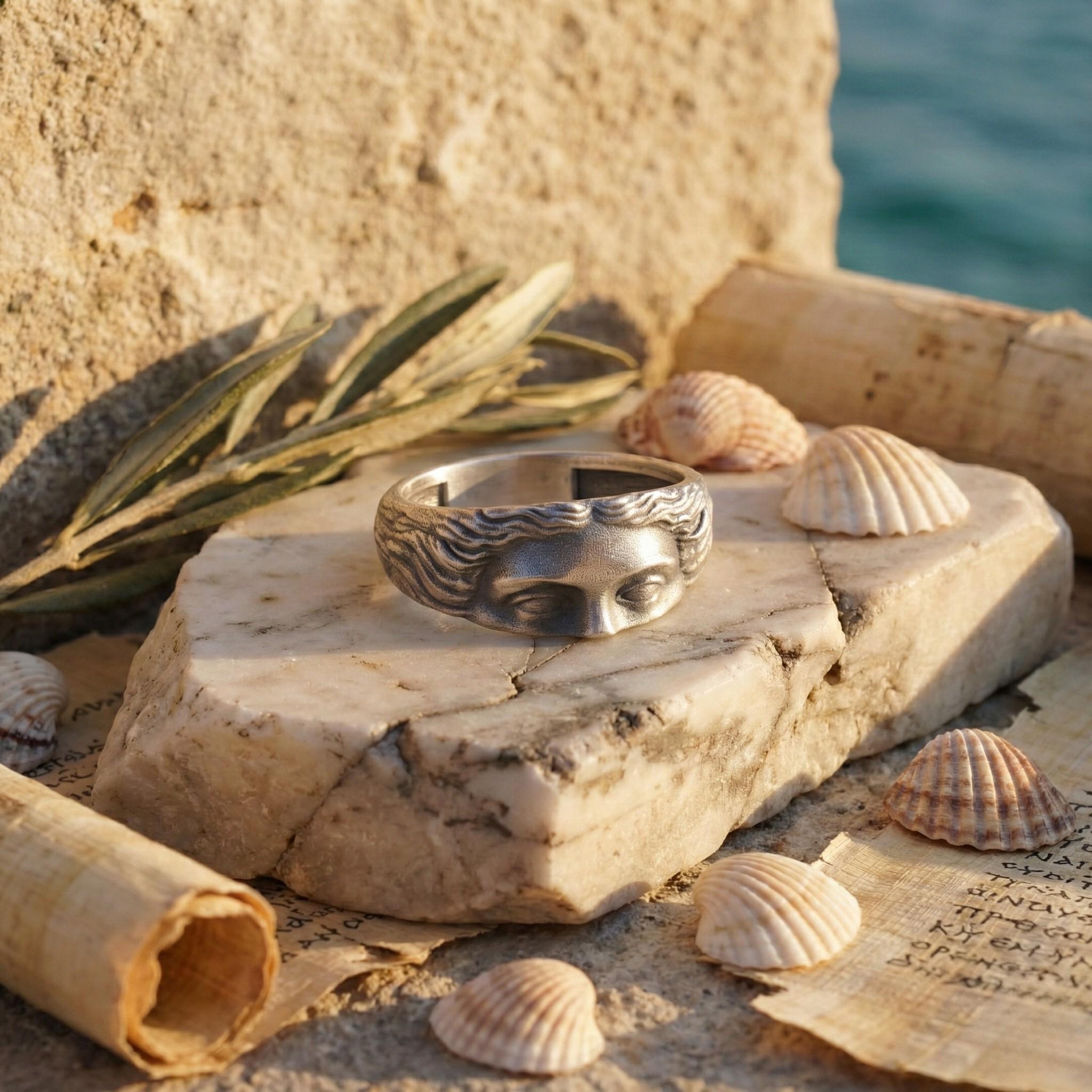 a ring with a face design, placed on a rock, surrounded by seashells and a scroll.