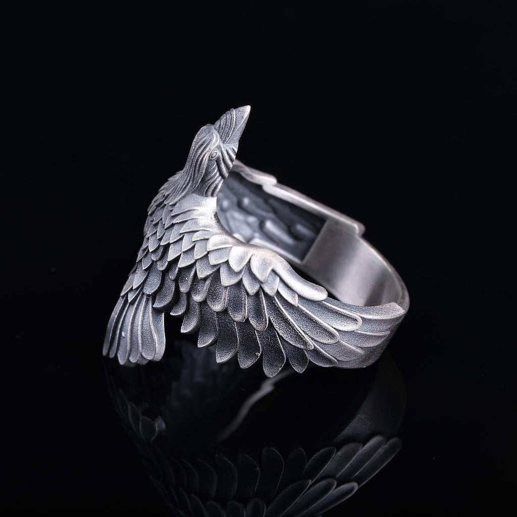 A silver-colored metal ring with a bird-like design, featuring a detailed wing-like pattern.
